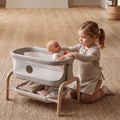 Young child placing a baby doll into the Maxi-Cosi Iora toy bassinet on the living room floor.