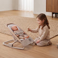 Lifestyle view of a young girl engaging in pretend play with a baby doll resting cozily inside the Maxi-Cosi Kori Doll Rocker.