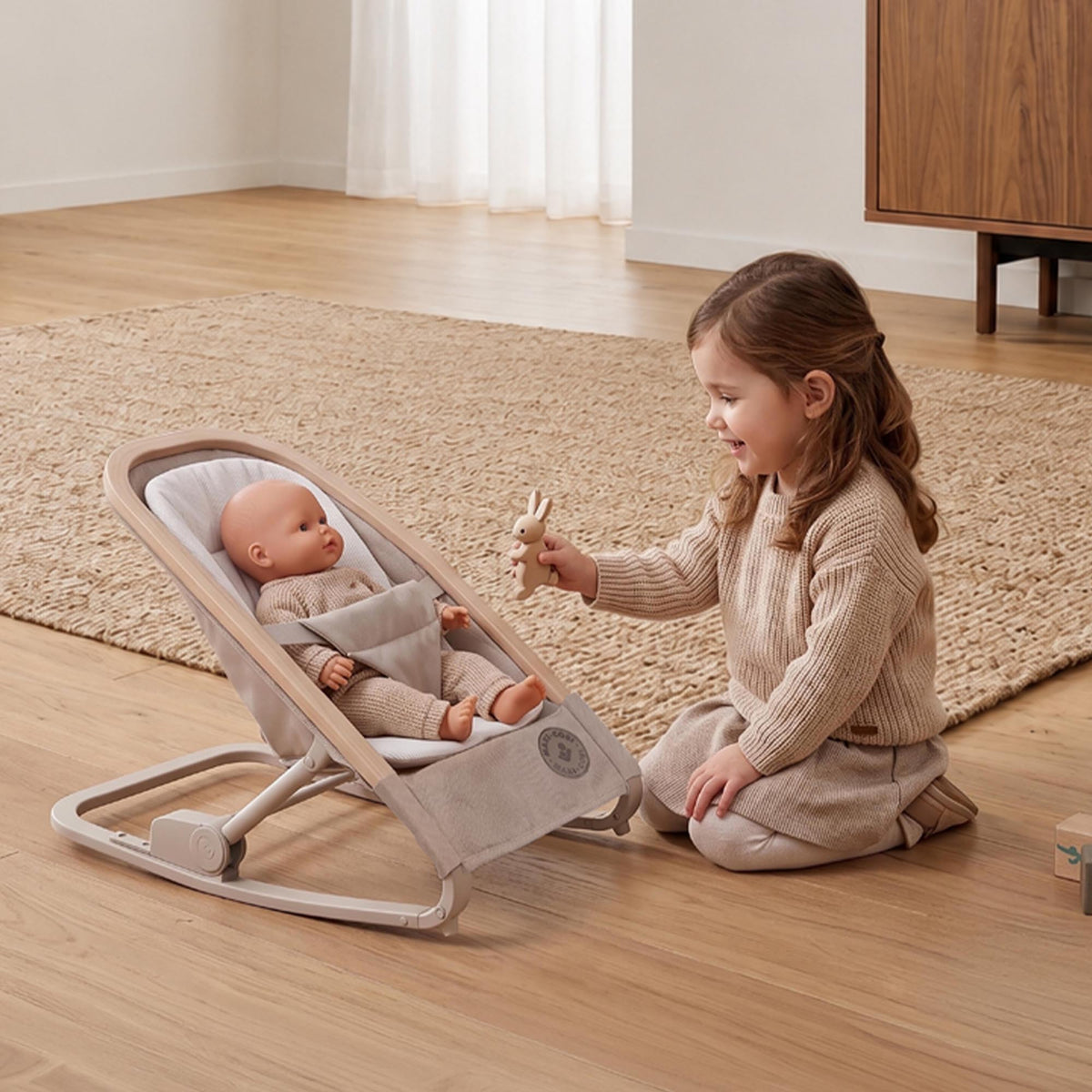 Lifestyle view of a young girl engaging in pretend play with a baby doll resting cozily inside the Maxi-Cosi Kori Doll Rocker.