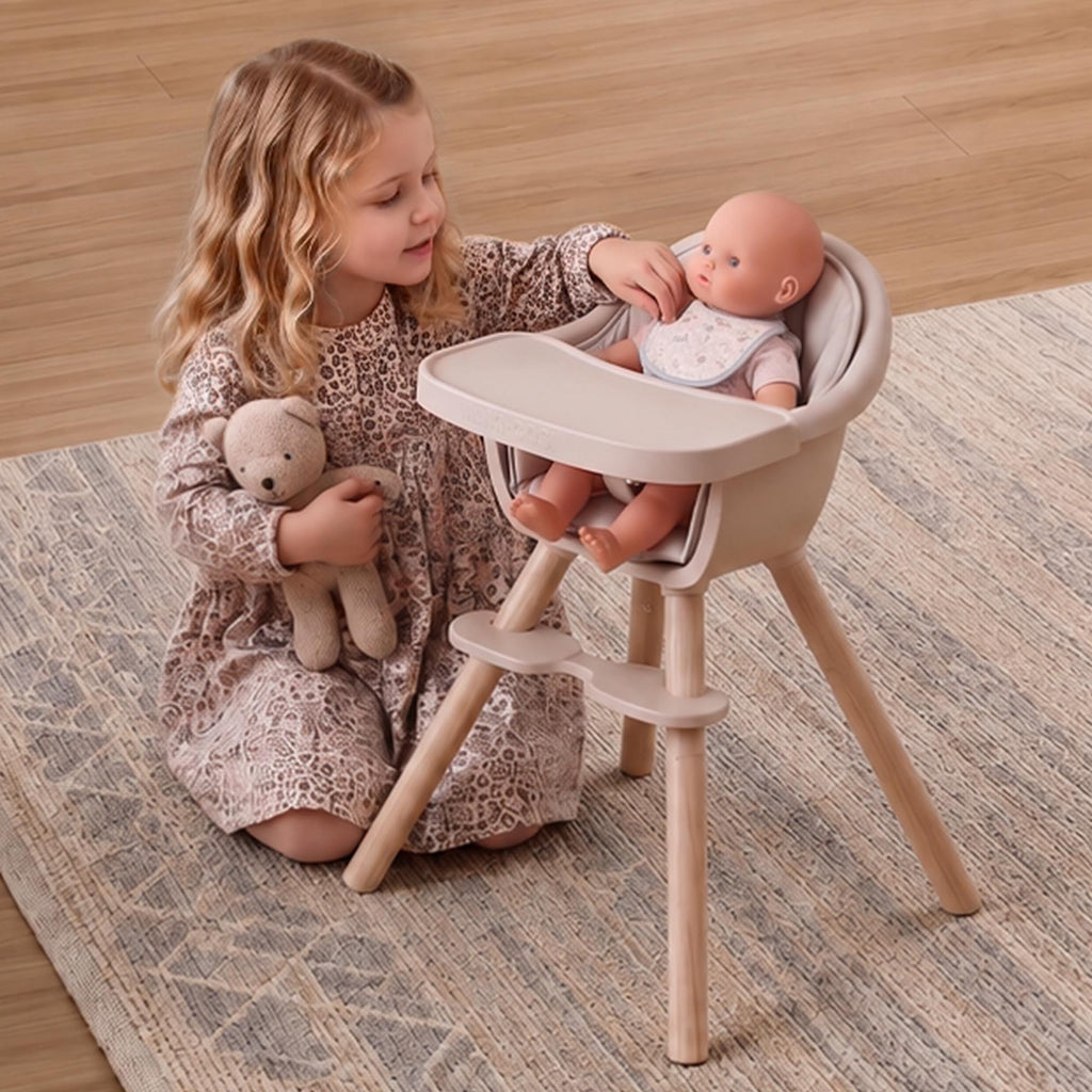 Young child seated on a rug feeding an 18-inch baby doll in the Maxi-Cosi Moa toy high chair.
