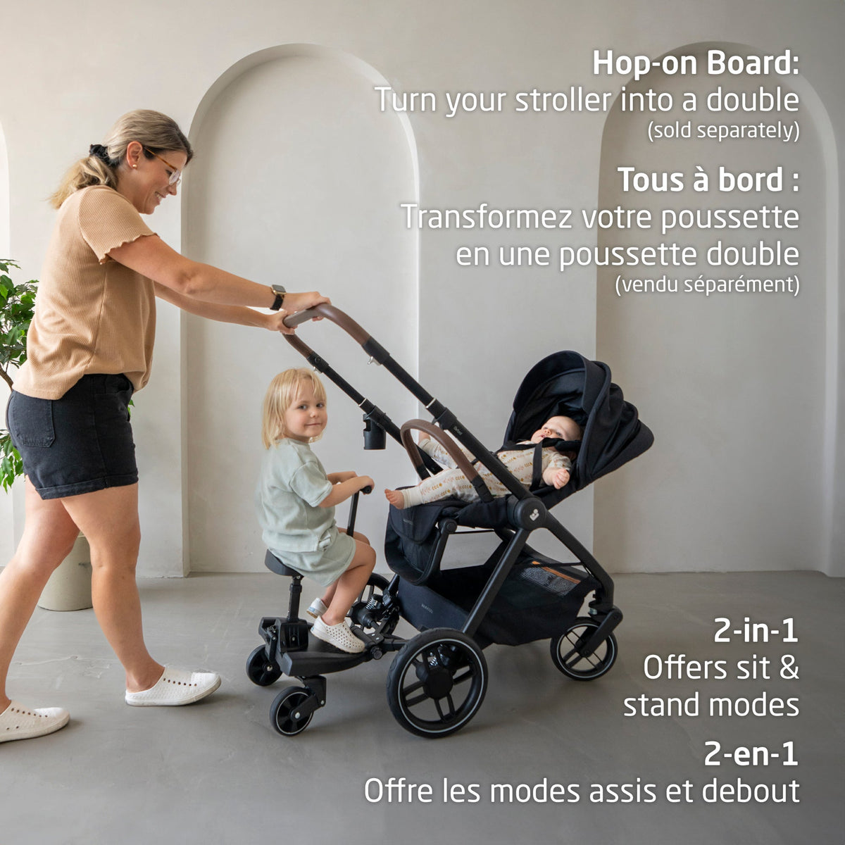 Lifestyle view of a mother pushing the Oxford stroller with baby while an older child rides the 2-in-1 sit and stand hop-on board attachment, turning the stroller into a double setup.